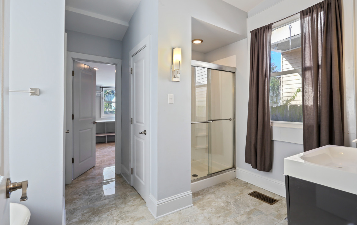 Bathroom with glass shower door, sink, and brown curtains on window