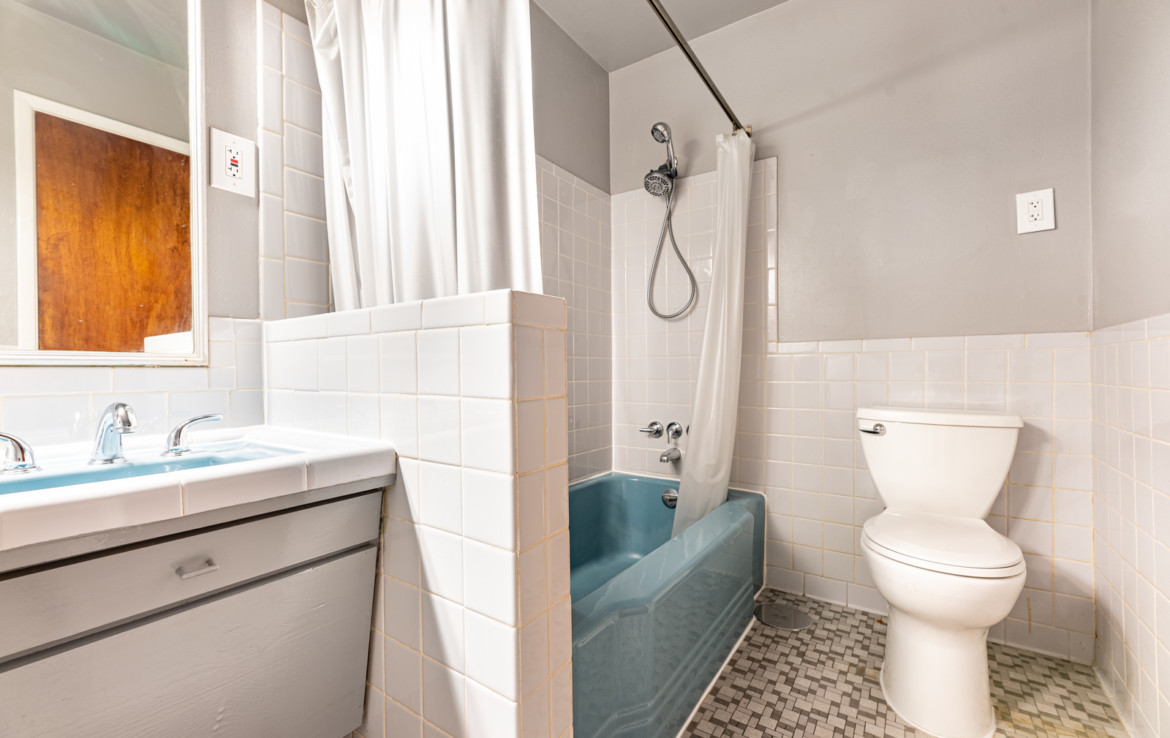 White tiled bathroom with toilet, sink and blue tub
